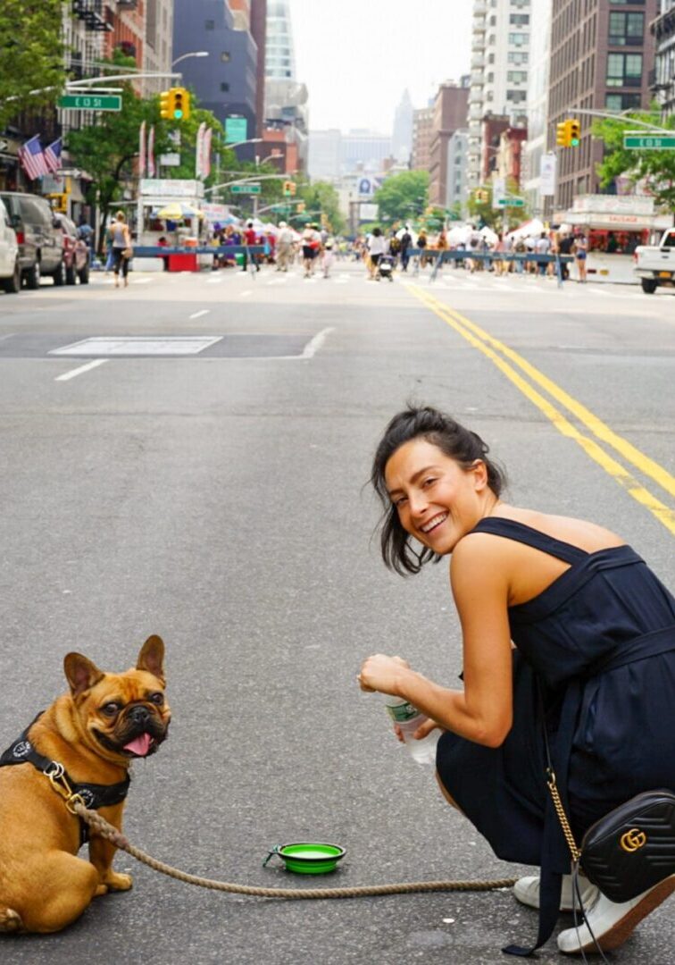 A woman kneeling down next to her dog on the street.