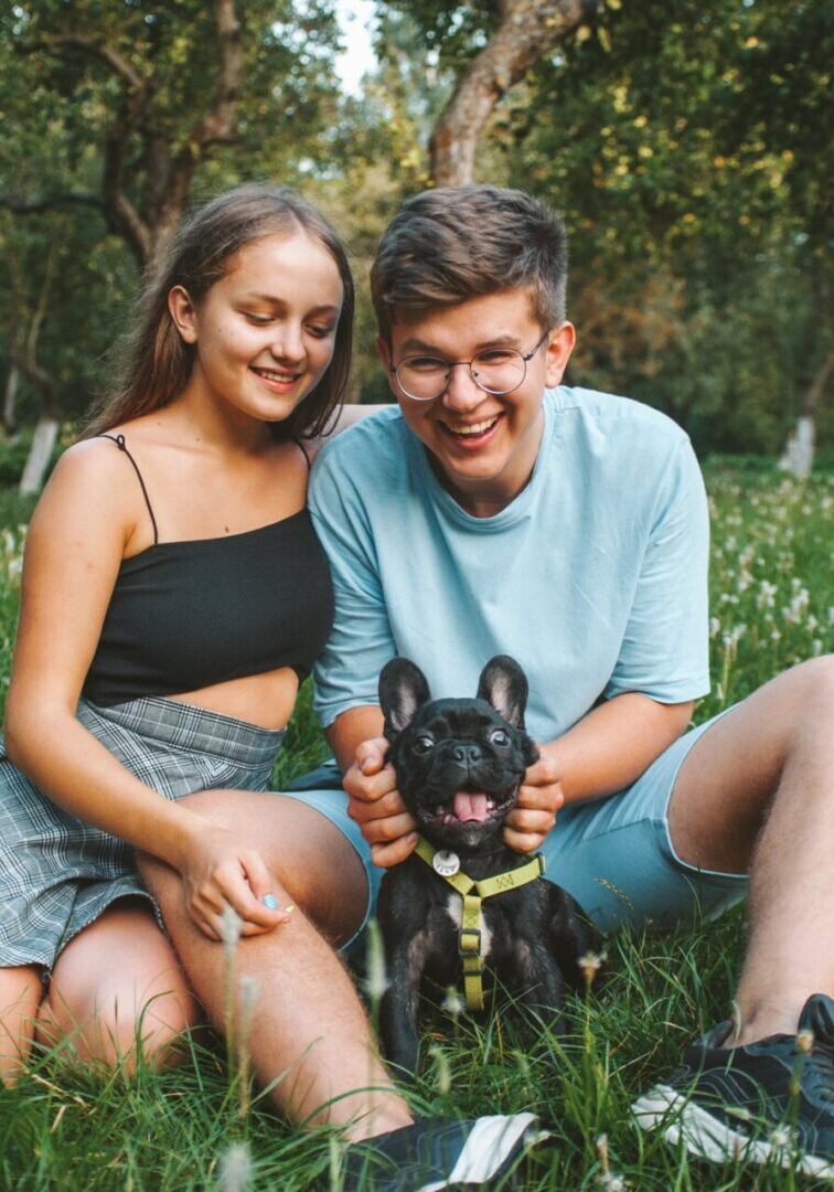 A man and woman sitting in the grass with their dog.